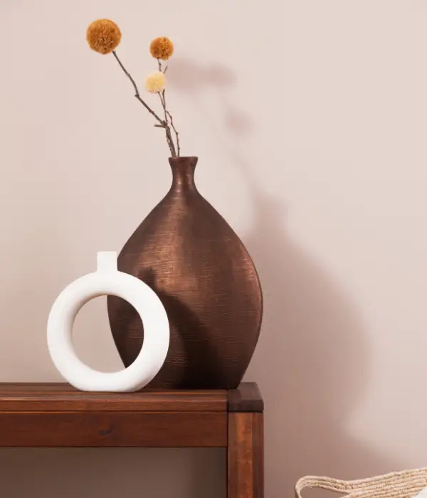 Brown and white decorative vases with pom pom stems on a wooden table.